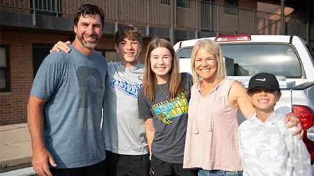 Freshman student smiling with family by dorm.