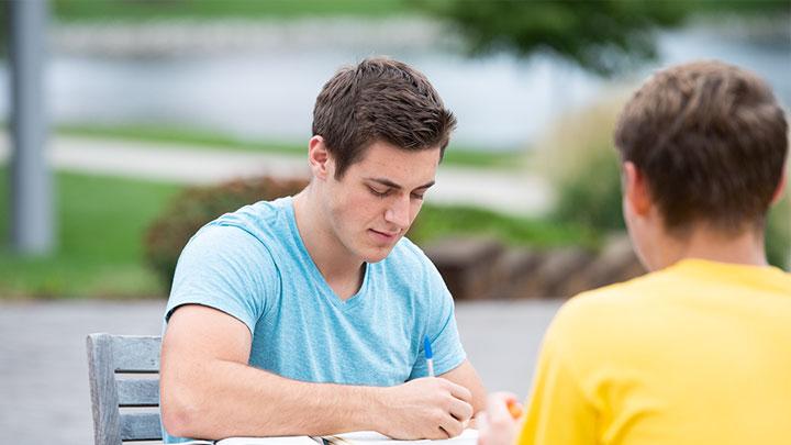 Two students studying at an outdoor table.